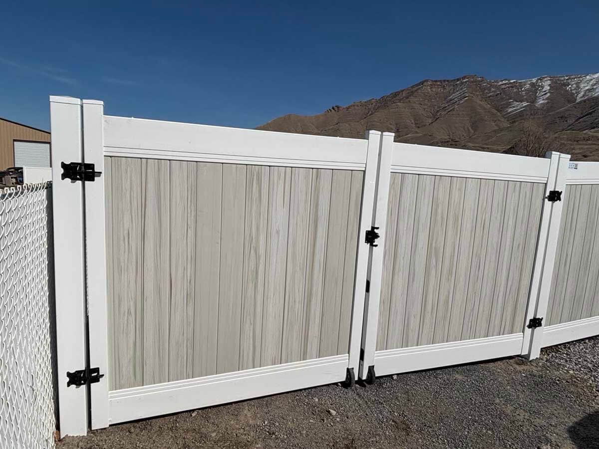White vinyl fence with black hinges and a closed gate beside a gravel yard, mountains in the background