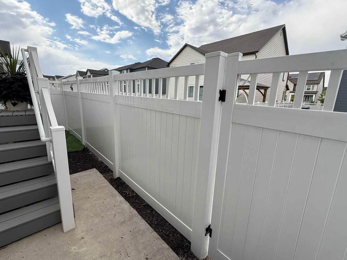 White vinyl fence with decorative top panels beside outdoor steps under a cloudy sky