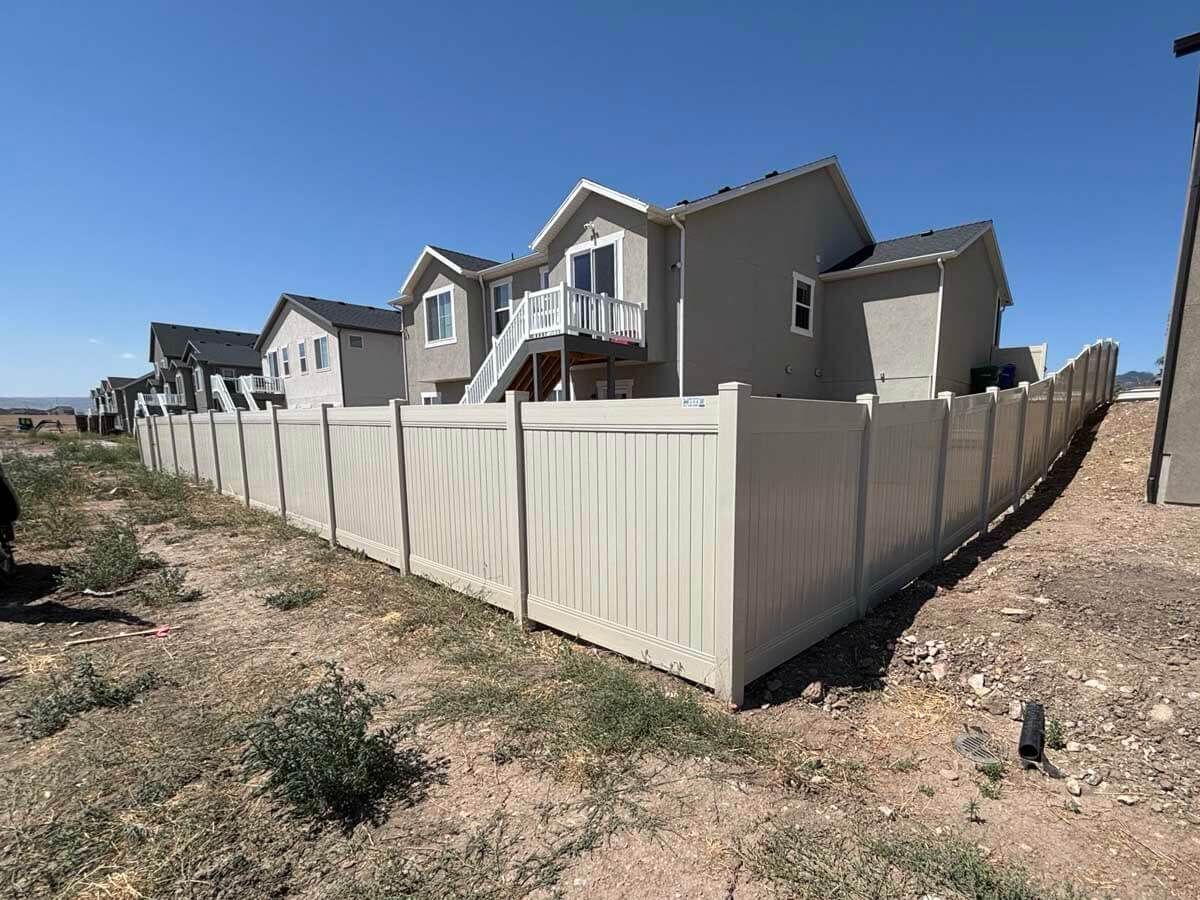 Suburban homes behind a white vinyl fence on a dry hillside under a clear blue sky