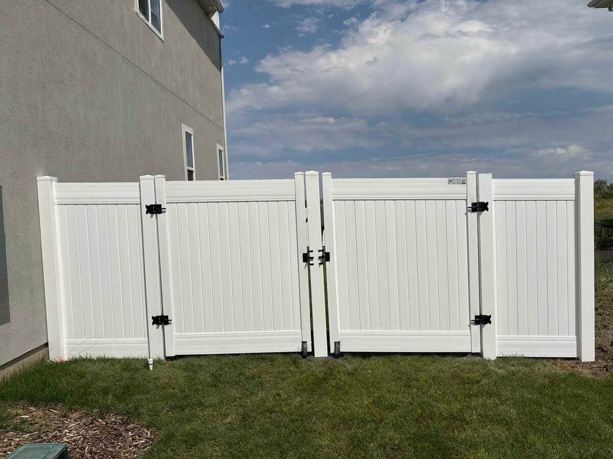 White vinyl privacy fence panels along a house side yard with grass and cloudy sky