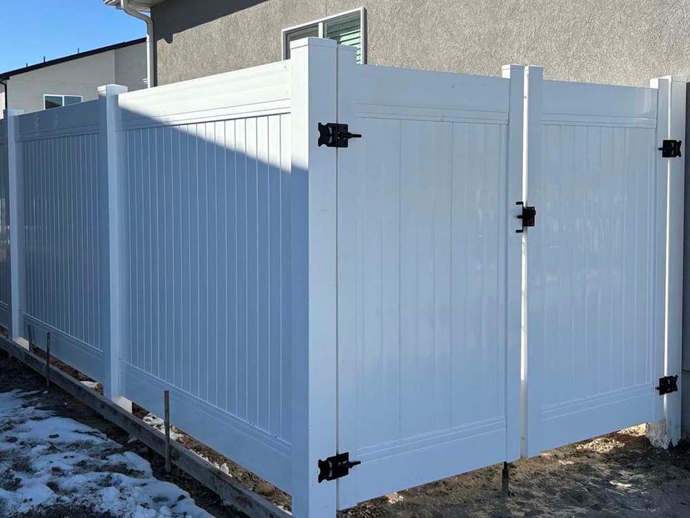 White vinyl privacy fence and gate beside a house in a snowy yard
