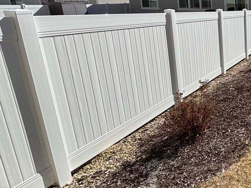 White vinyl fence beside a gravel strip with a small bare shrub in front of houses