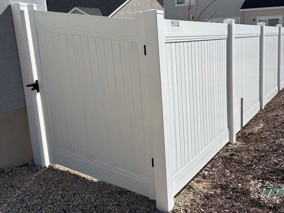 White vinyl privacy fence corner with a gate, set along a gravel yard.