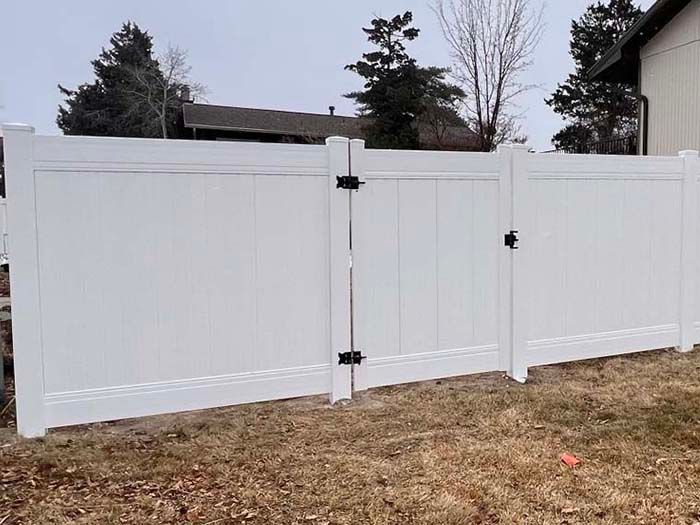 White vinyl privacy fence with a matching gate in a grassy yard.