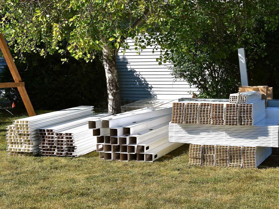 Stacks of white PVC pipes and wire mesh panels on grass in front of a shed