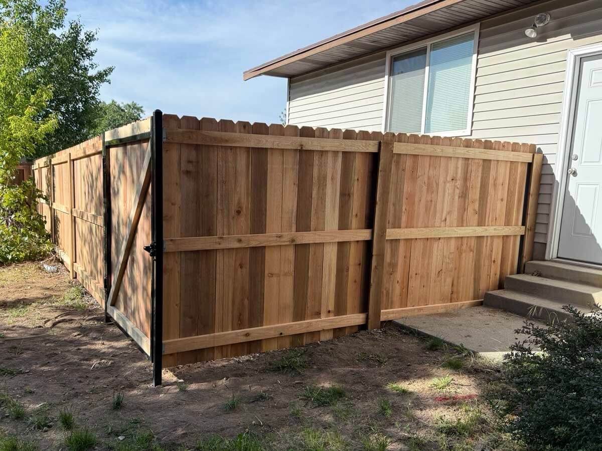 Wooden privacy fence enclosing a side yard beside a beige house with a sliding glass door.