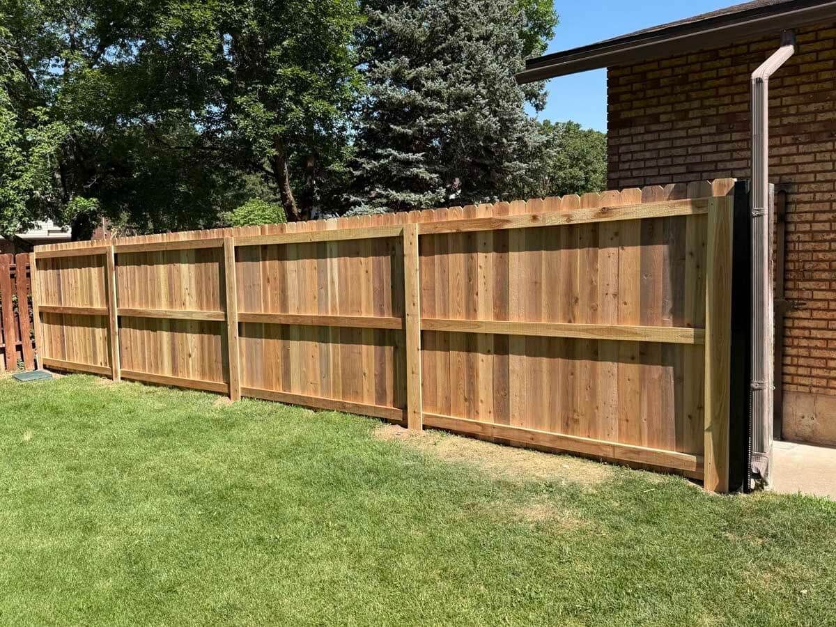 Wooden privacy fence along a grassy backyard beside a brick house and trees