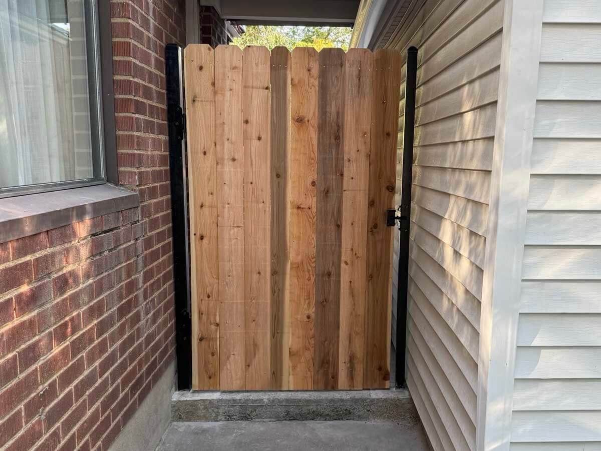 Narrow outdoor passage with a wooden gate between a brick wall and vinyl-sided house