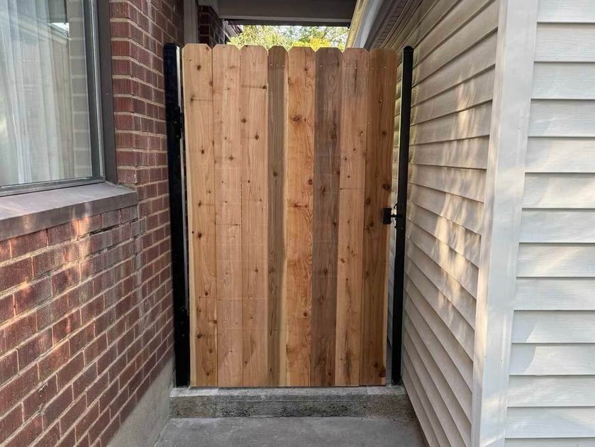 Wooden gate closing a narrow outdoor passage between a brick wall and a house siding