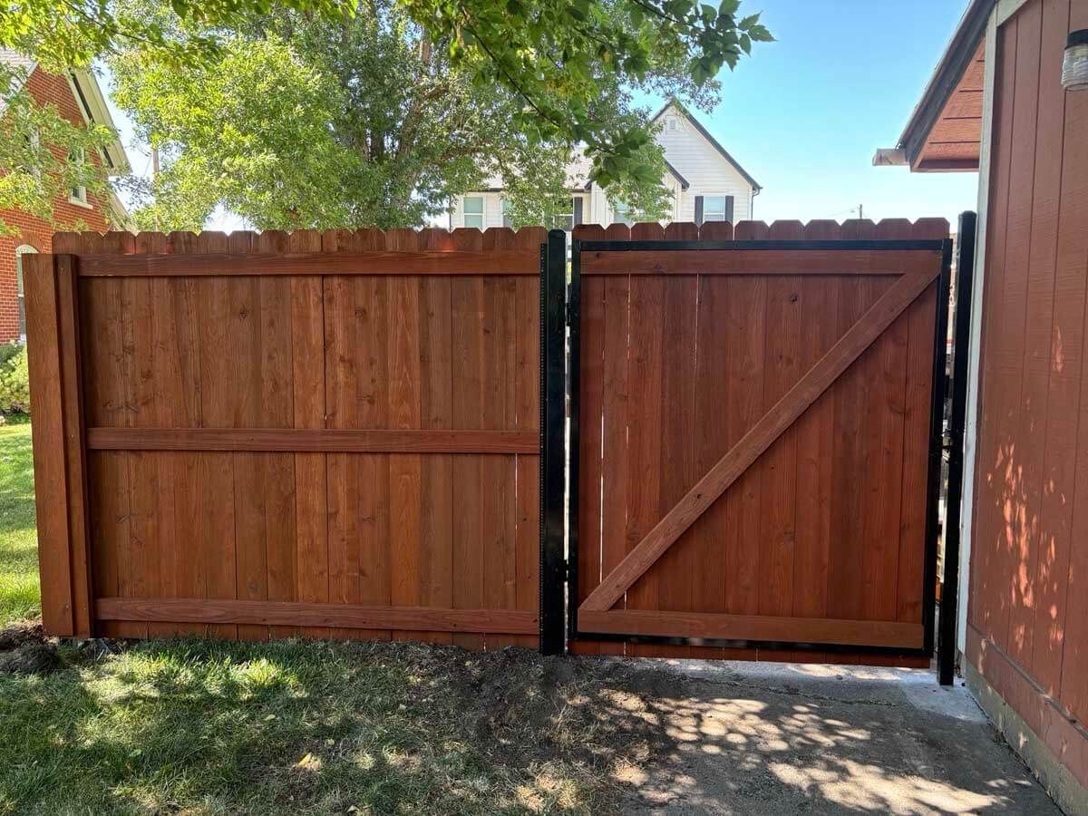 Wooden double gate in a backyard, with a tree overhead and a brick wall on the right.