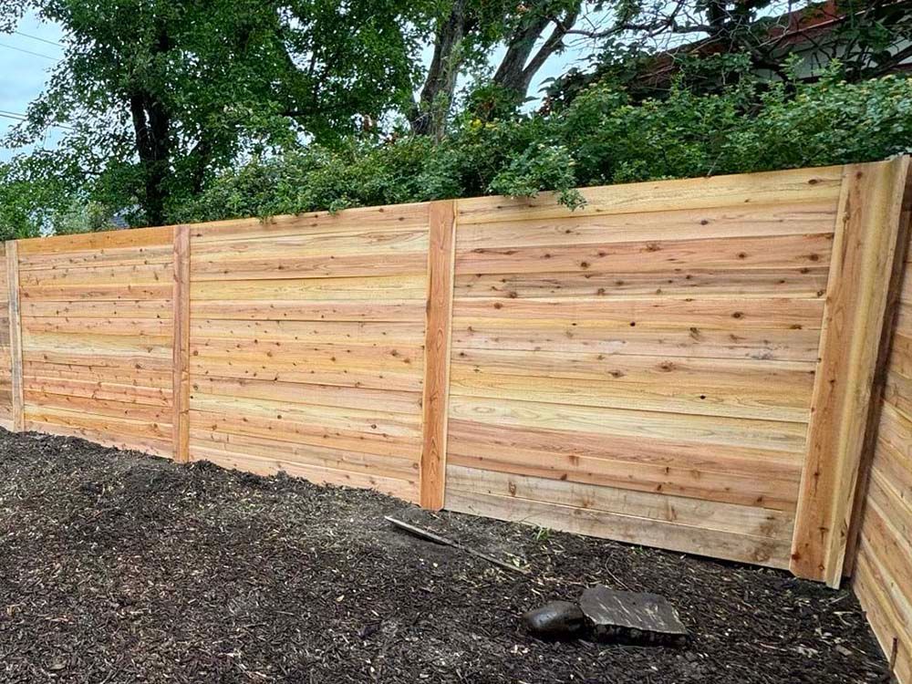 Wooden privacy fence along a gravel path with trees and greenery behind it