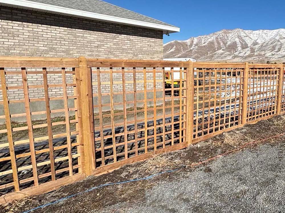 Wooden lattice fence beside a stone building, with mountains in the background.