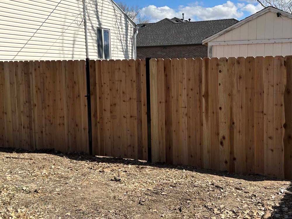 Wooden privacy fence with a closed gate in a residential backyard under a partly cloudy sky