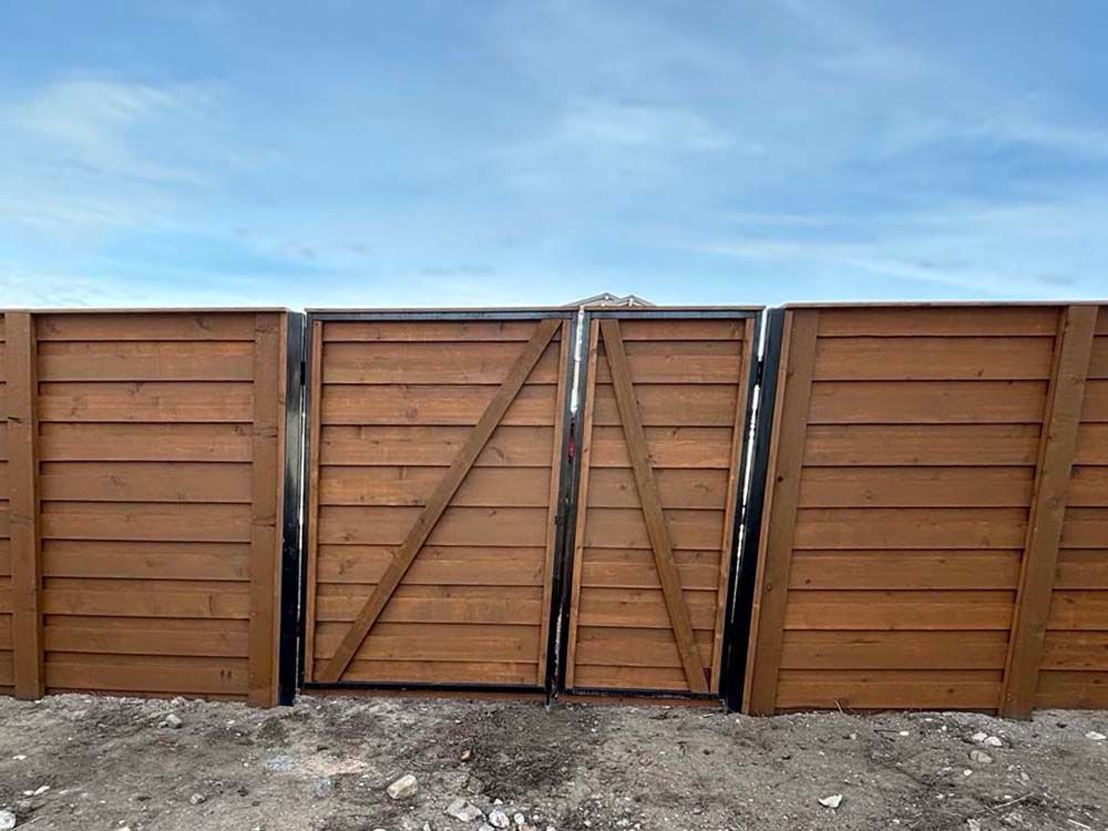 Brown wooden fence with a damaged central gate under a blue sky