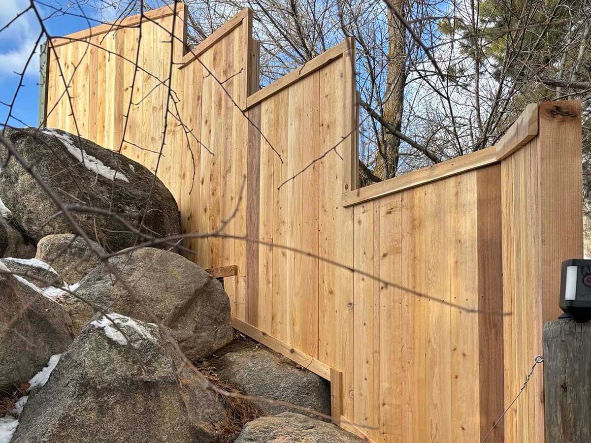 Wooden fence with a zigzag top beside large rocks and trees on a hillside