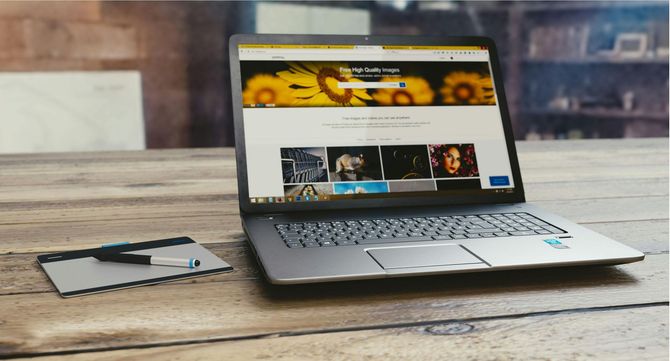 A laptop displaying a webpage with sunflower imagery rests on a wooden table beside a small drawing tablet and pen.
