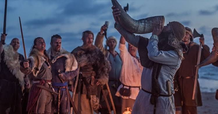 A group of vikings are standing on a beach holding swords and axes.