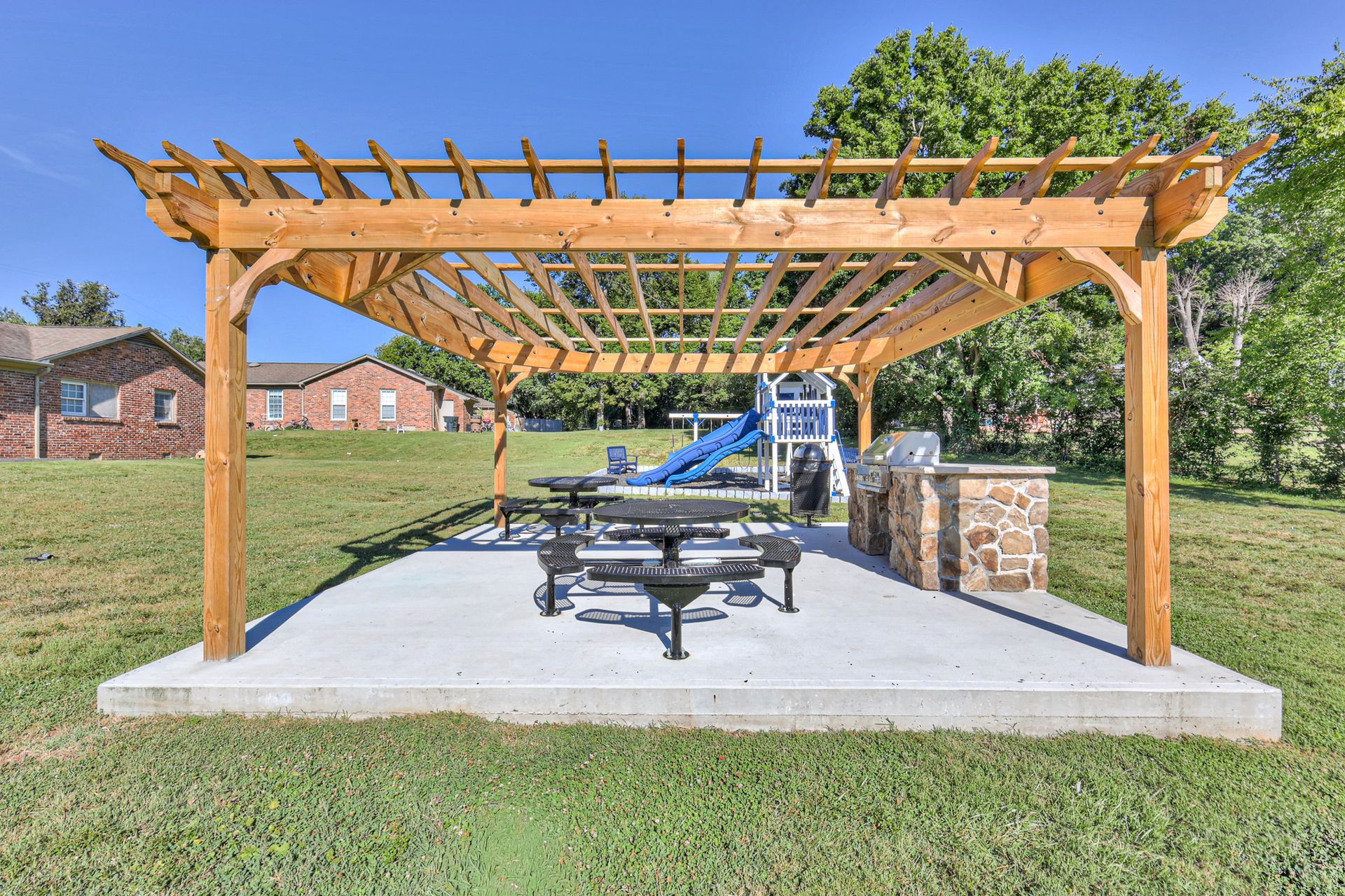 Photo of a community grill area, showing the platform it's on, a seating area, and the playground in the background