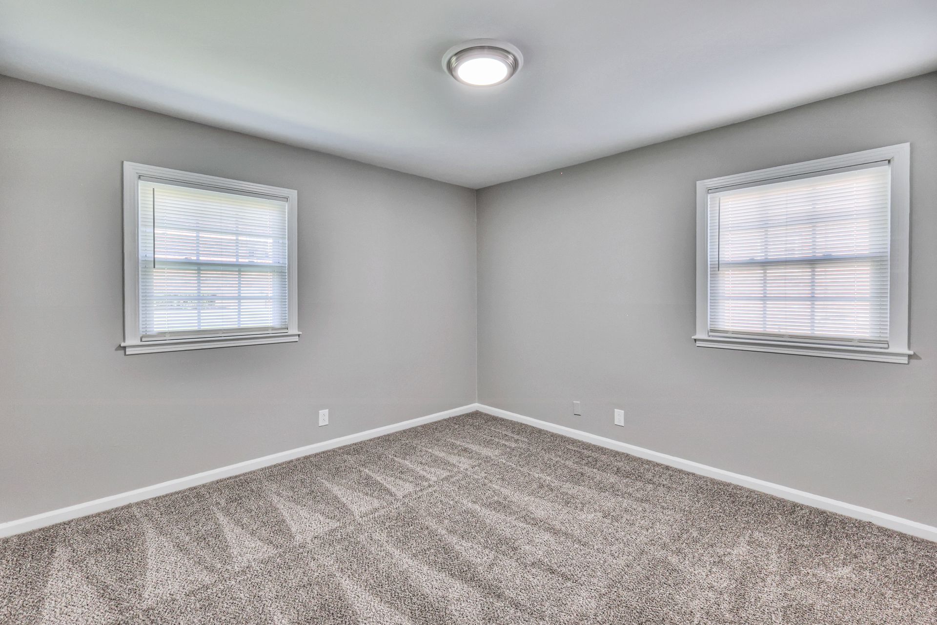 Photo of a bedroom with two conjoining walls, each wall having a window