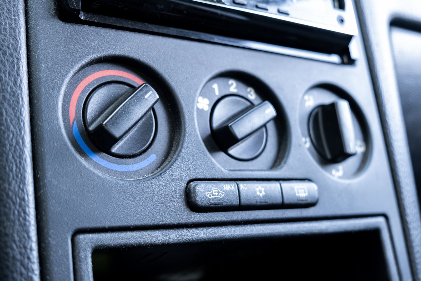 Car's dashboard with three black knobs for climate control: temperature, fan speed, and direction.