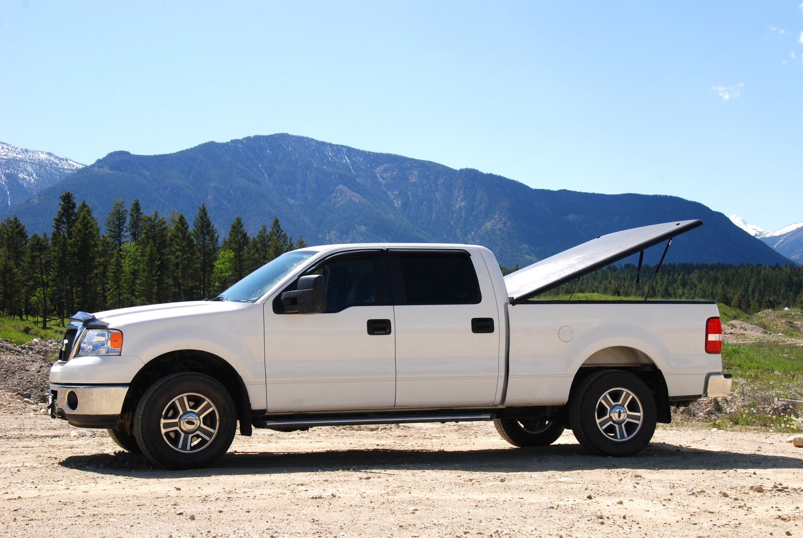 White pickup truck with bed cover open, set against a mountain backdrop.
