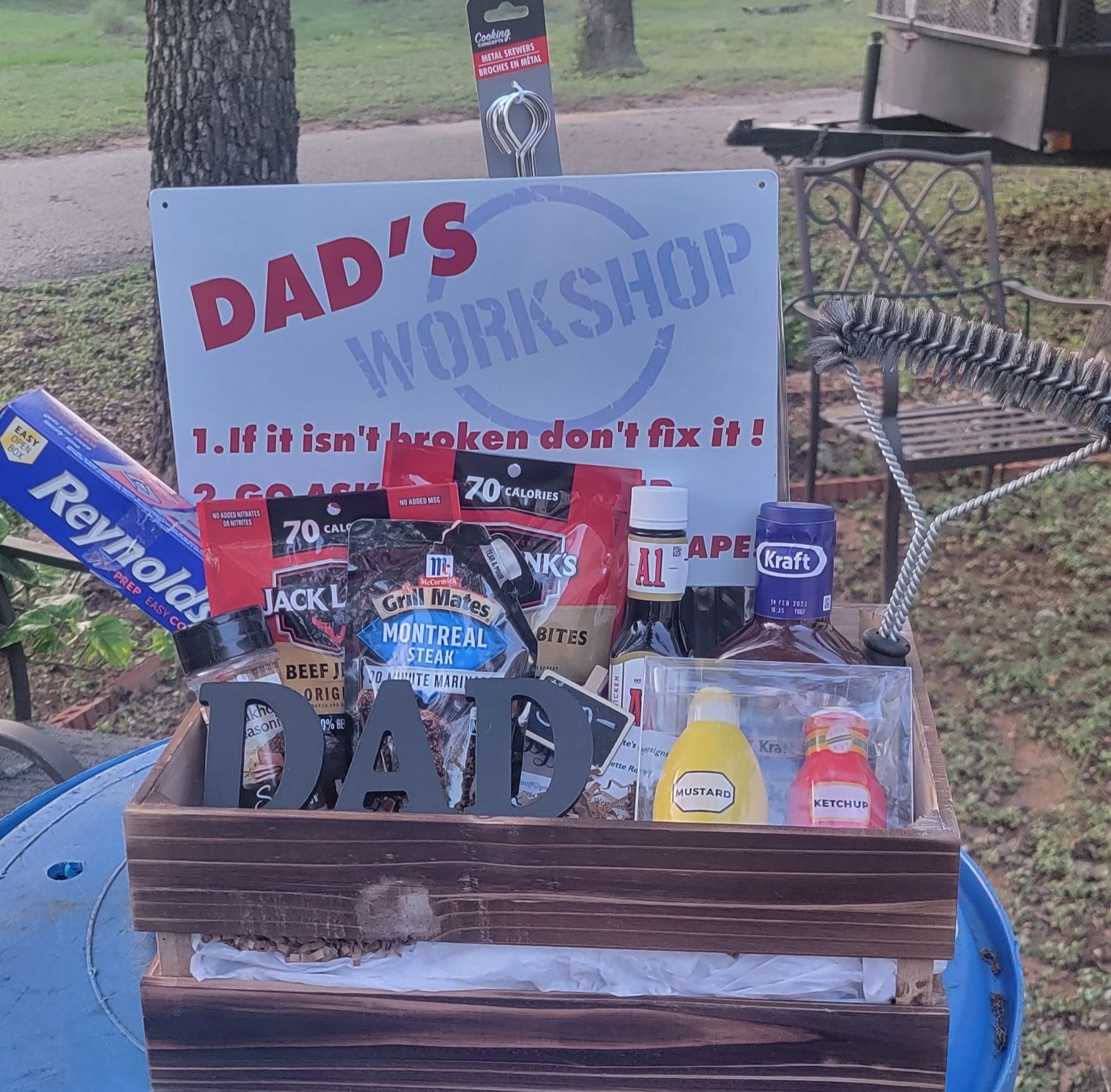 Dad’s Workshop sign with tools, bottles, and a decorative metal chair on a table outdoors