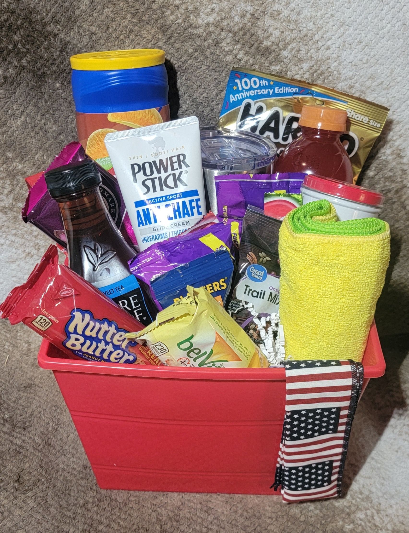 Red gift basket filled with assorted snacks, drinks, and cleaning items in bright packaging.