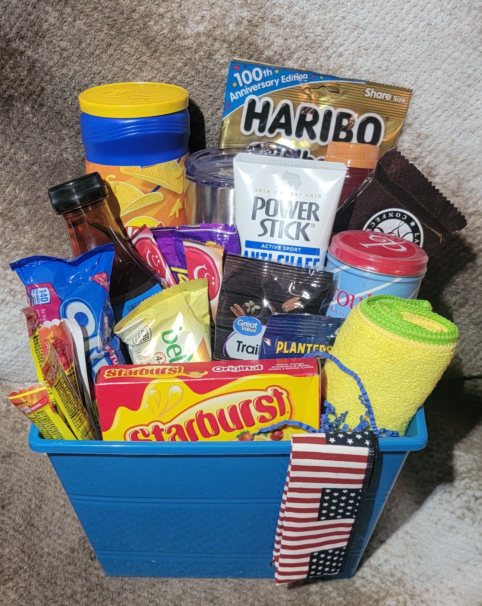 Blue container filled with assorted snacks and candy, including Haribo, Power Stick, and Starburst packages.