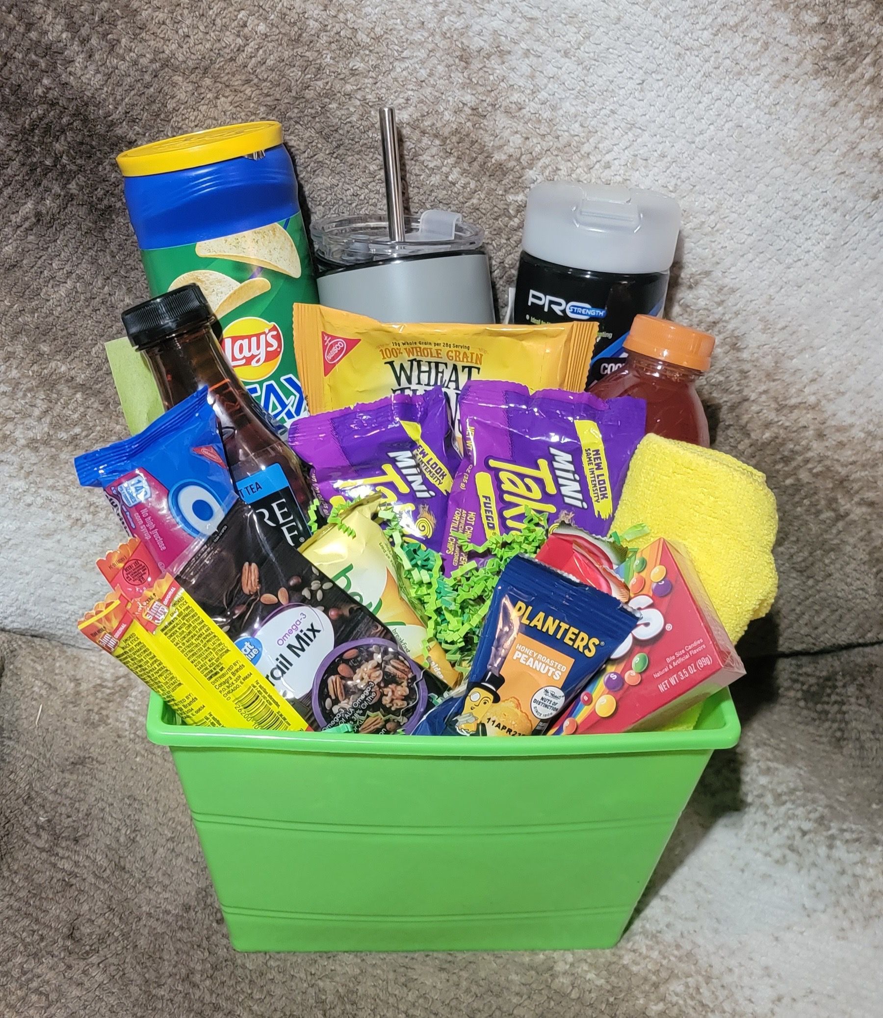A green bin filled with assorted colorful snack packages and household items on a countertop.