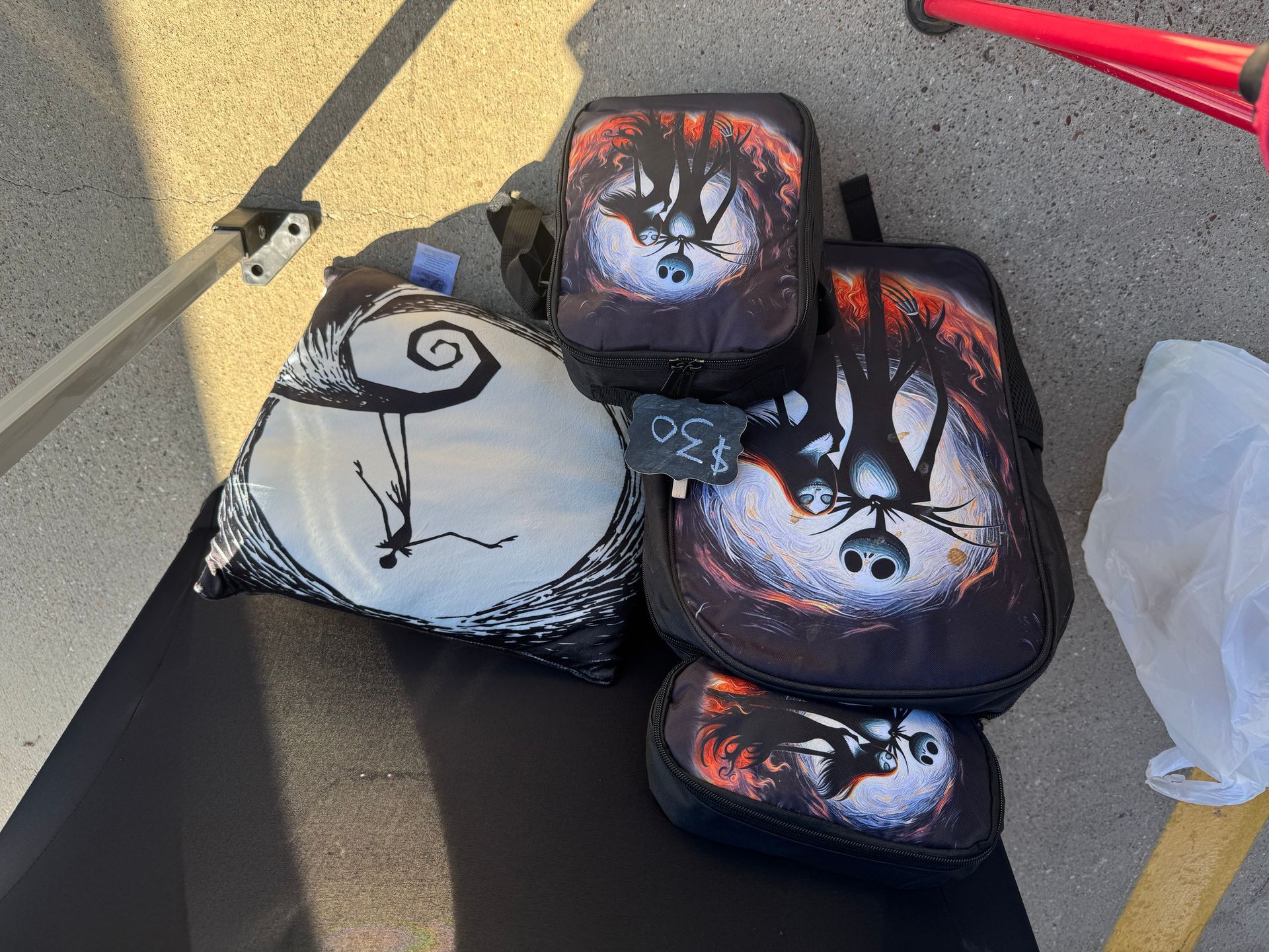 Stacked bags with Jack Skellington faces on a sidewalk near a red stroller handle.