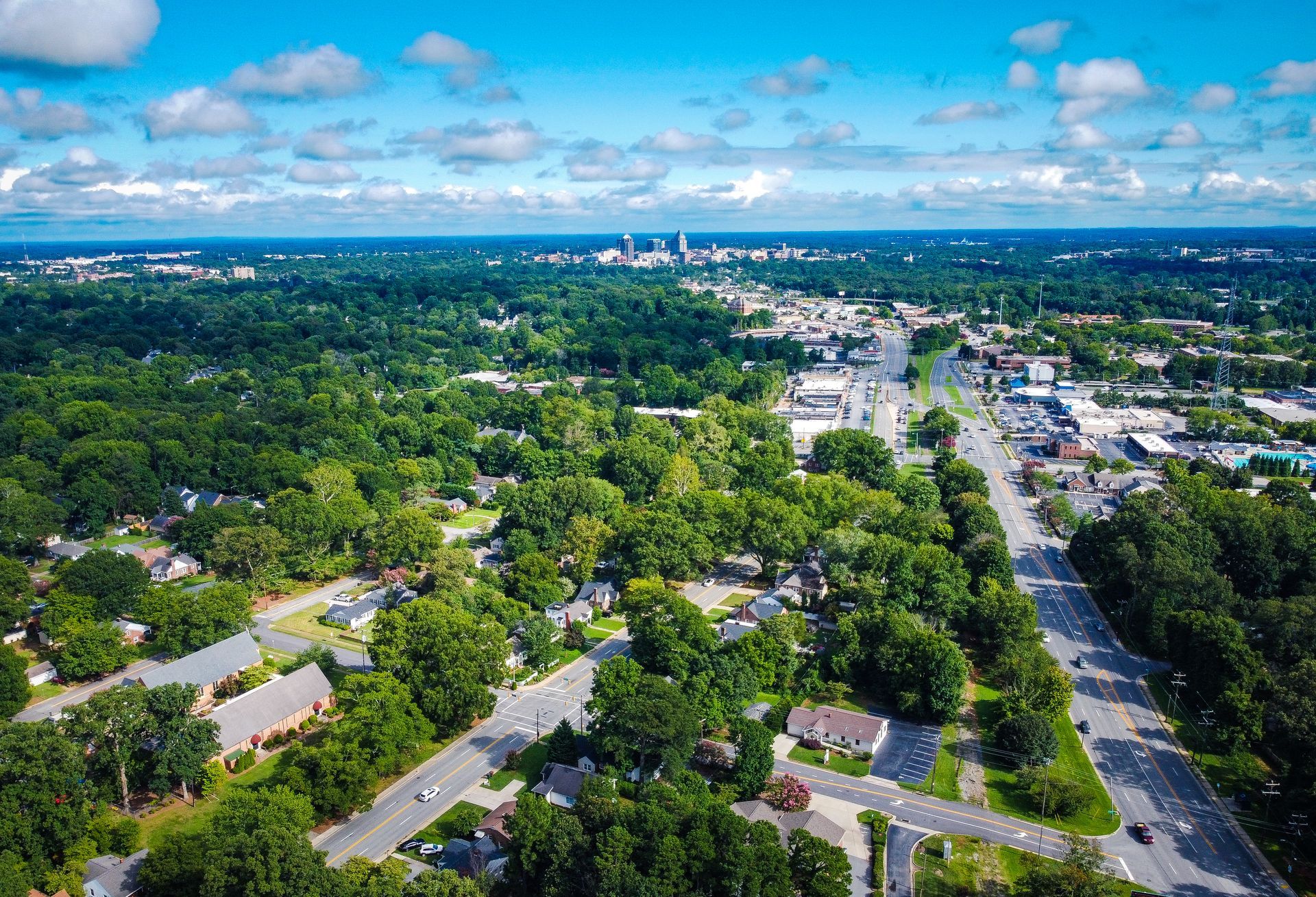 Aerial view of Fort Mill, SC with roads, houses, and a distant Charlotte city skyline under a blue sky.