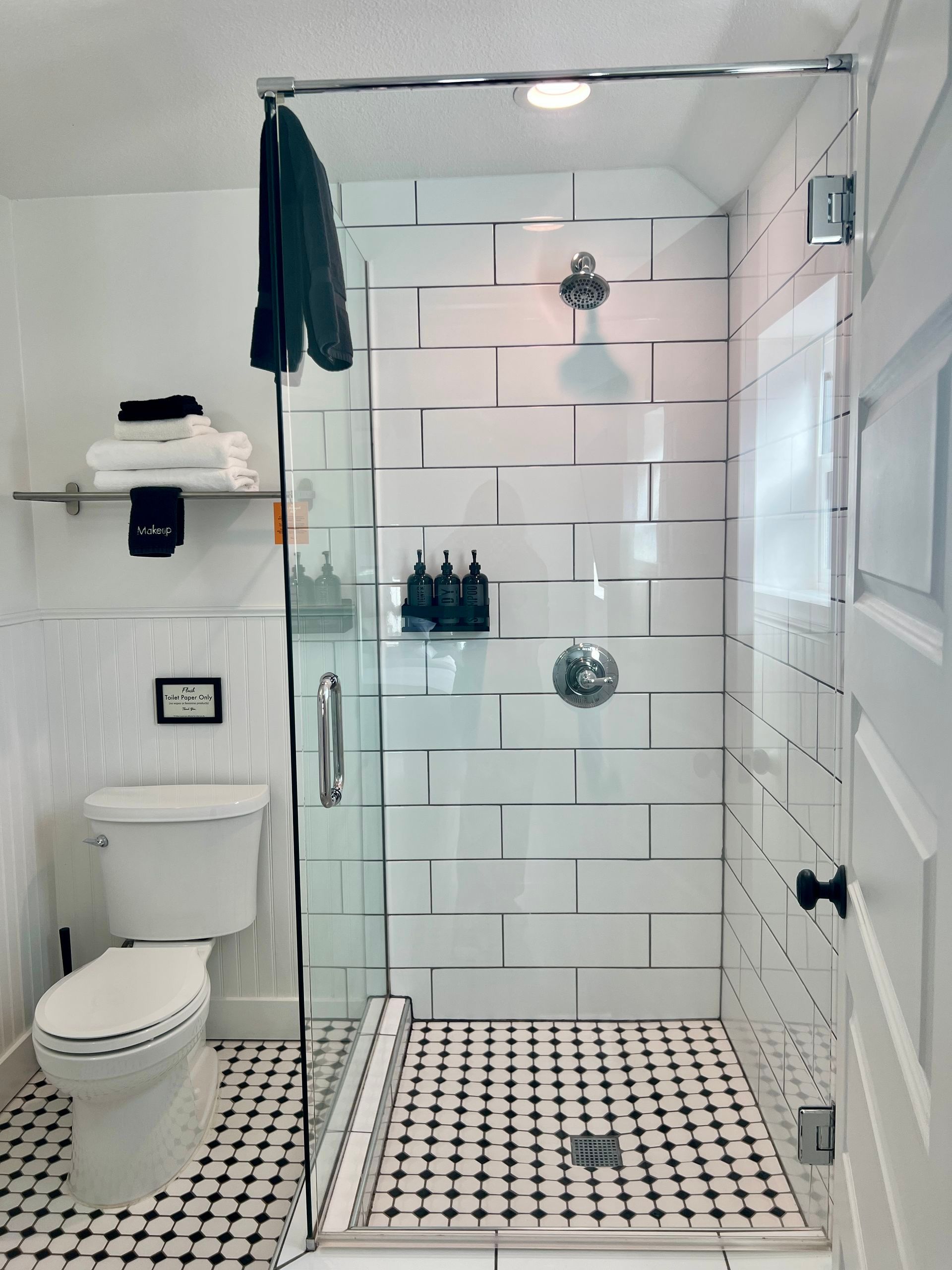 Modern white bathroom with glass shower, black and white tile floor, and white subway tile walls.