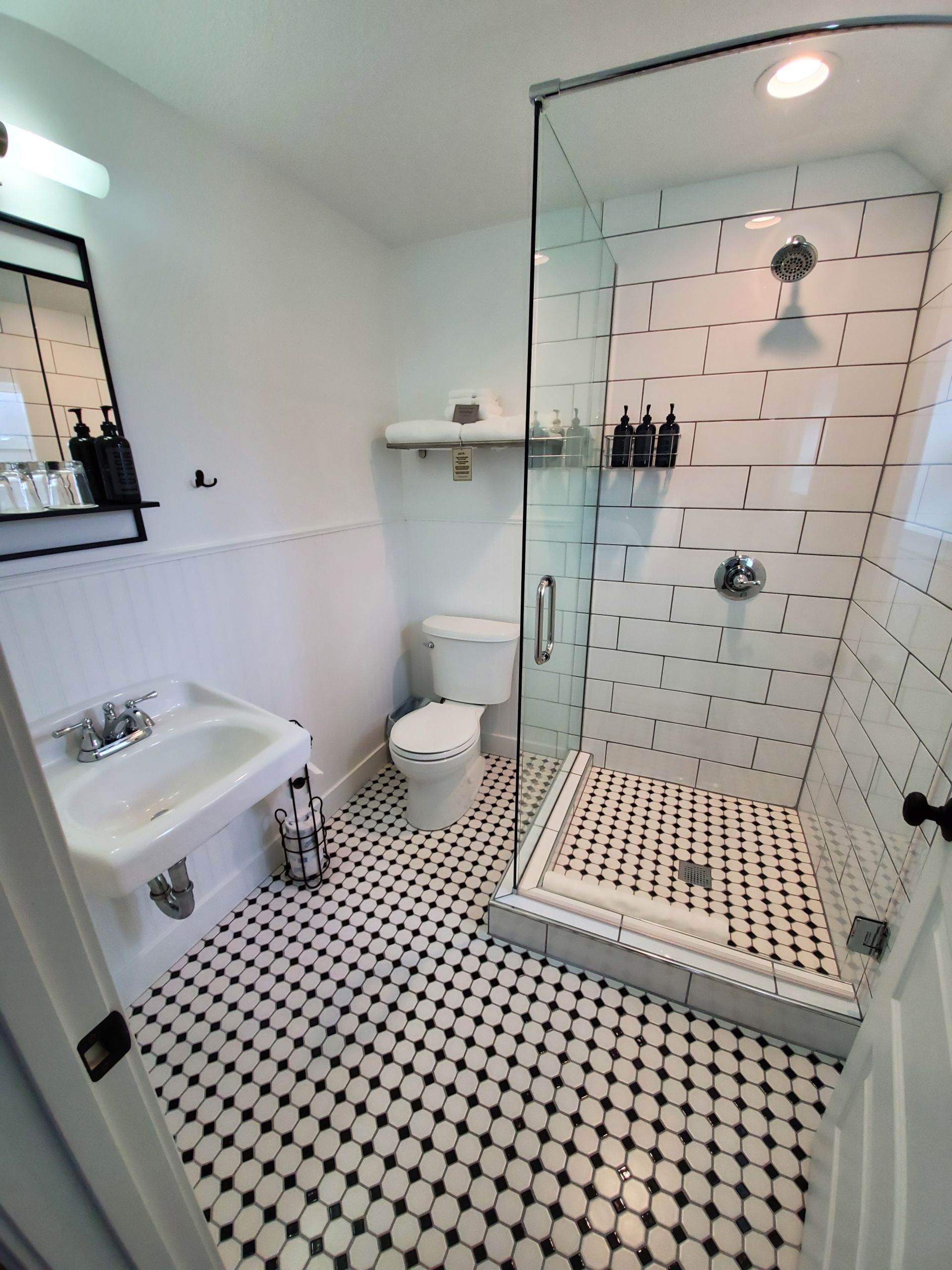 Black and white bathroom with tiled floor and shower. White walls. Sink and toilet are visible.