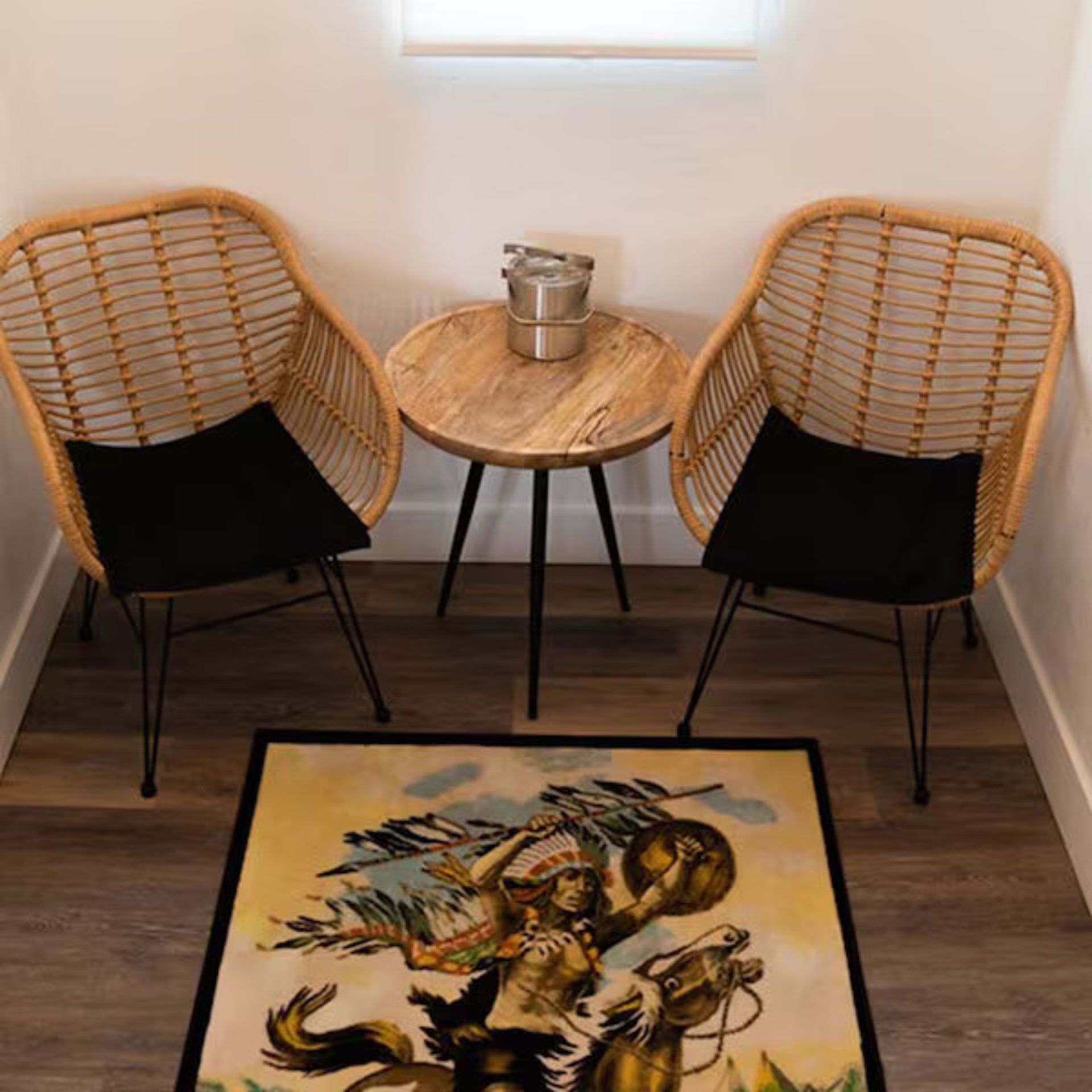 Two rattan chairs, small table, and rug with cowboy graphic in small room.