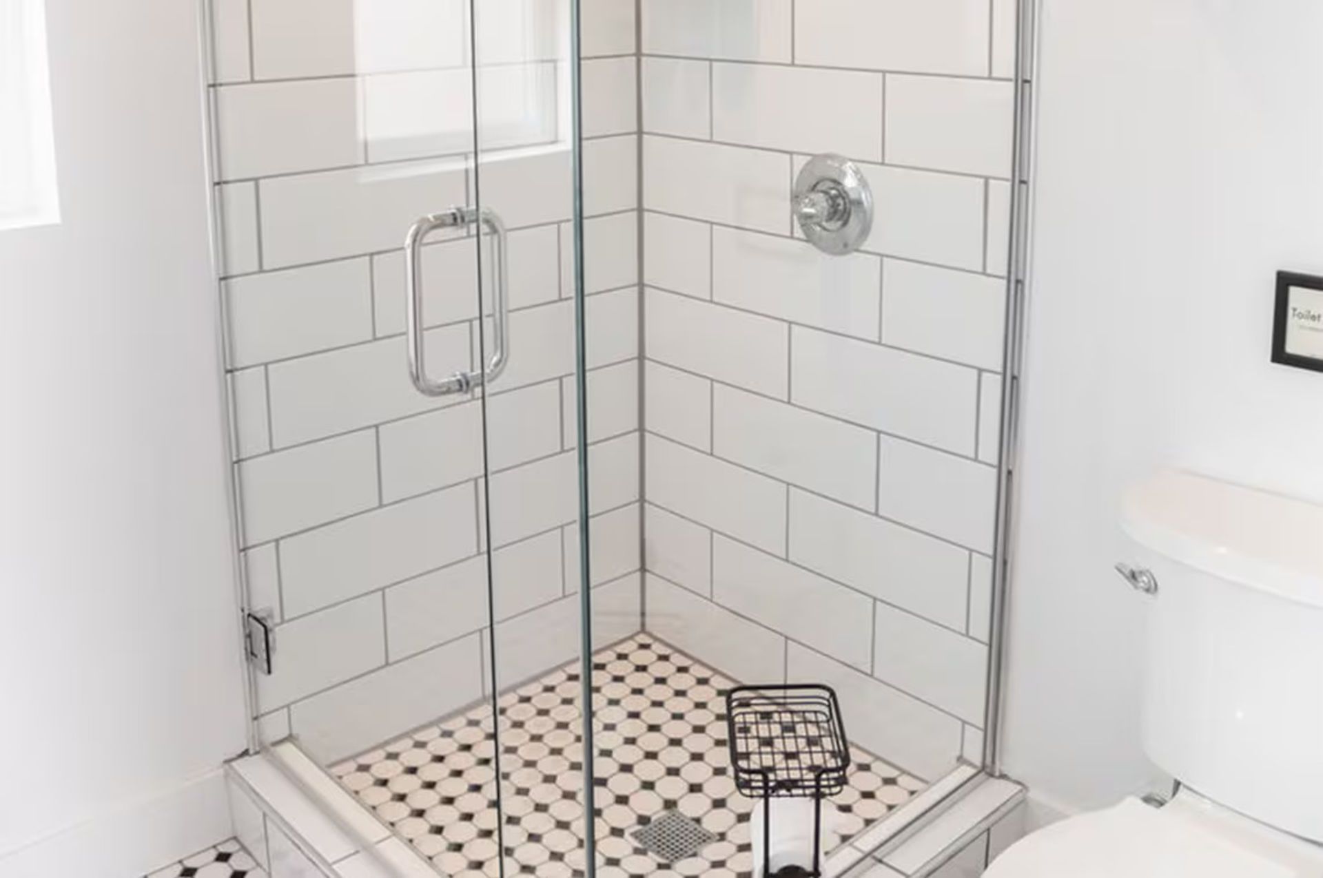 Shower with white subway tiles, glass doors, and a black and white patterned tile floor.