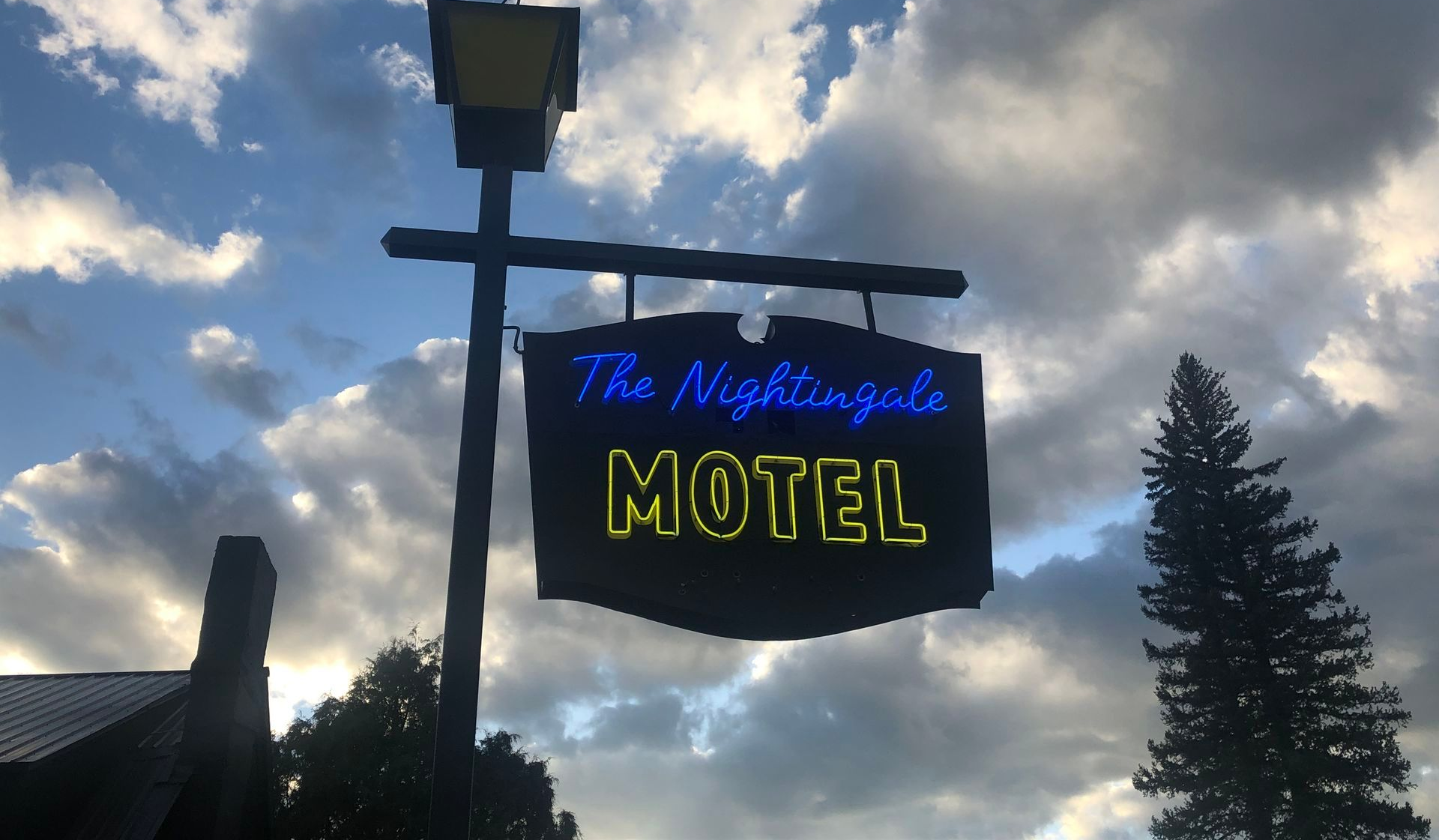 The Nightingale Motel sign against a cloudy sky. Blue and yellow neon.