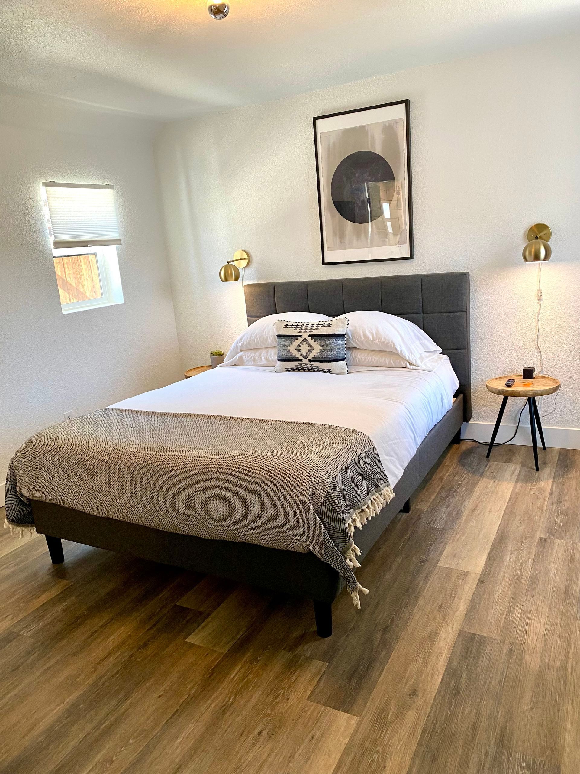 Cozy bedroom with bed, throw blanket, art, side table, and sconce lighting.