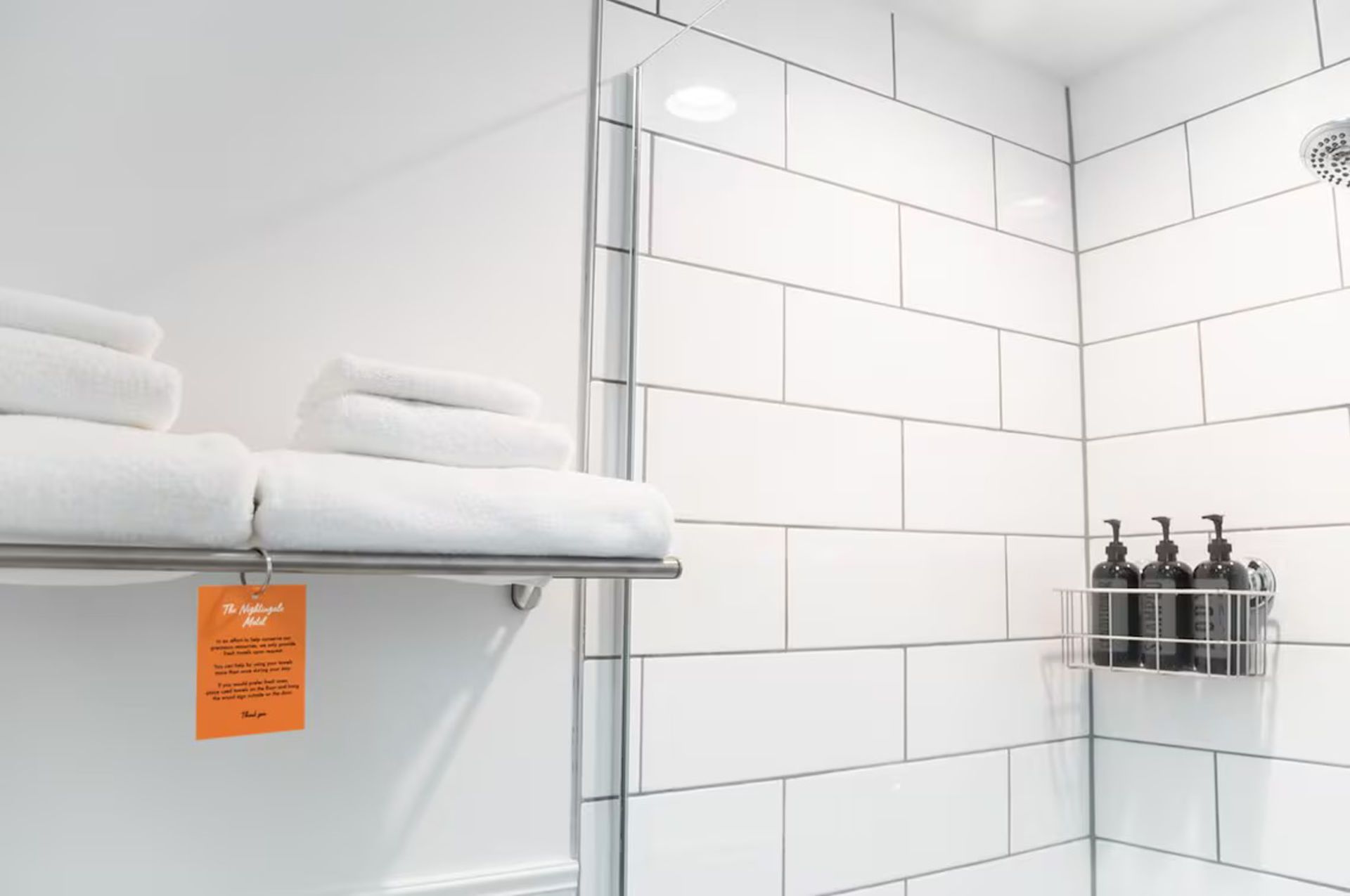 White tiled shower with towels on a rack and bottles in a wire caddy.
