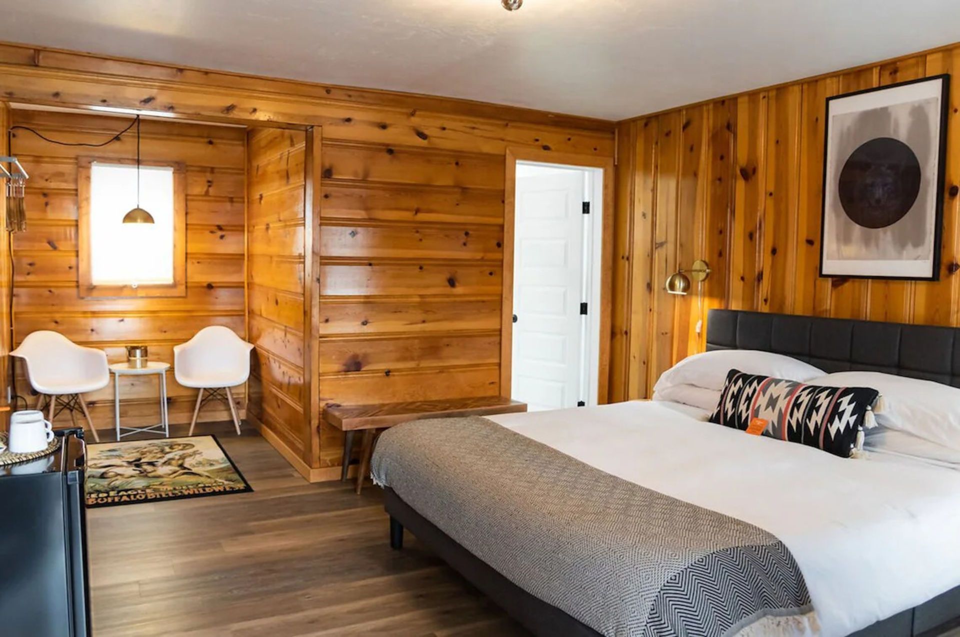 Cozy cabin bedroom with wood paneling, a bed, chairs, and art.