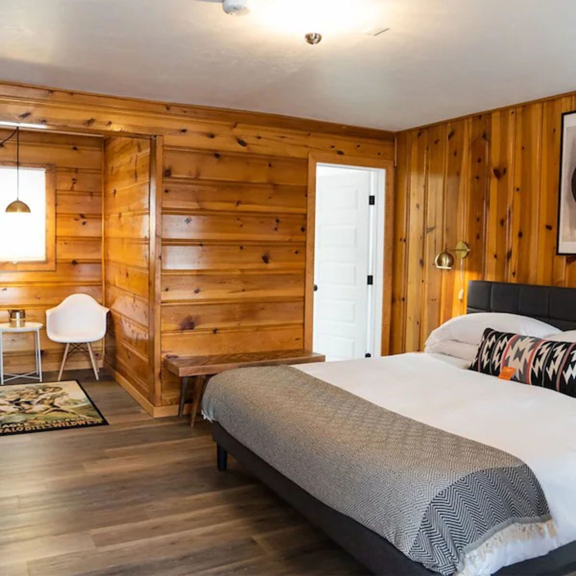 Wooden-paneled bedroom with a bed, white chair, and a door to a bathroom.