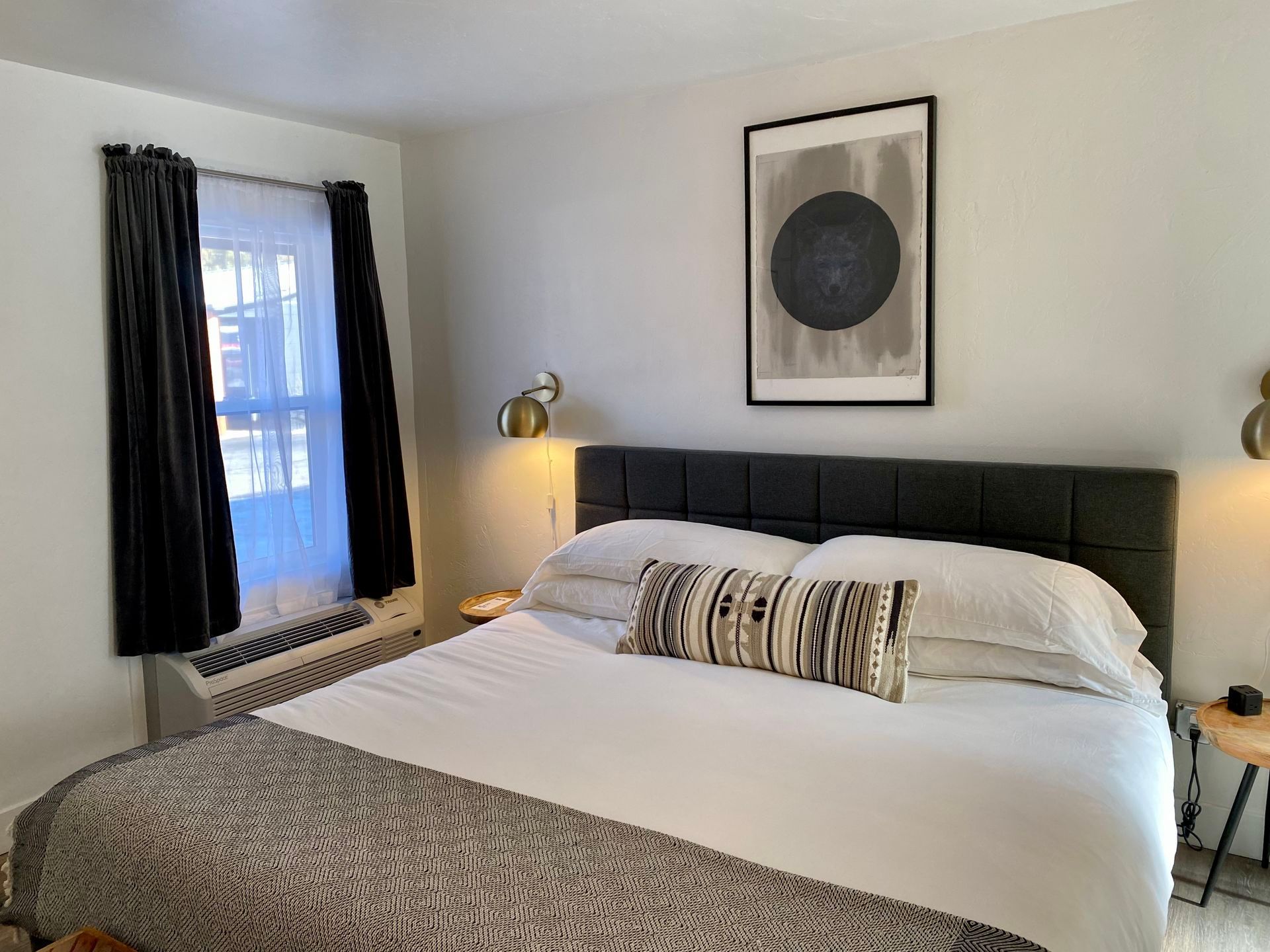 Bedroom with a bed, black curtains, and a piece of art on the wall.