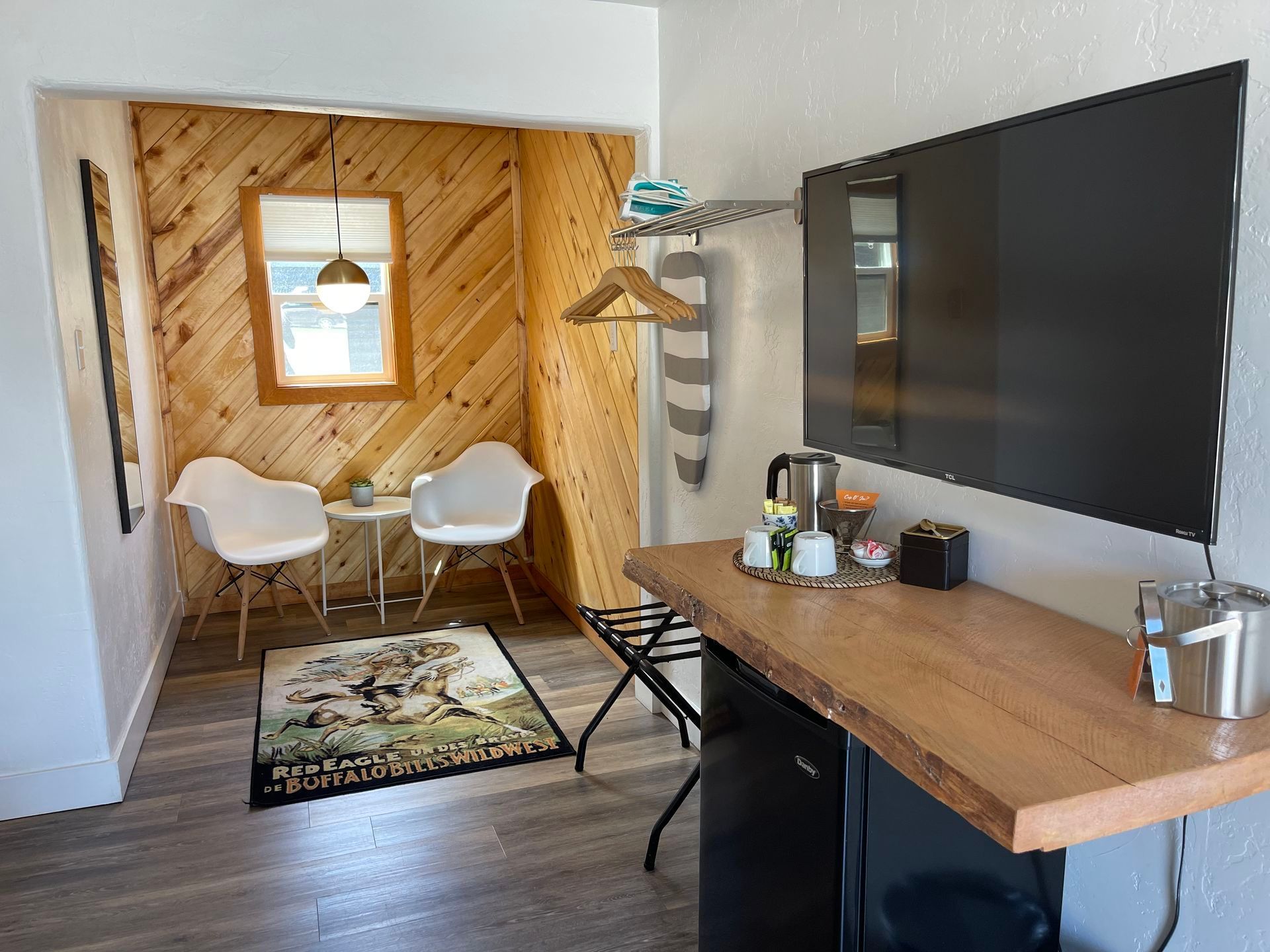 Cozy hotel room corner with seating area, TV, mini-fridge, and wood paneling.