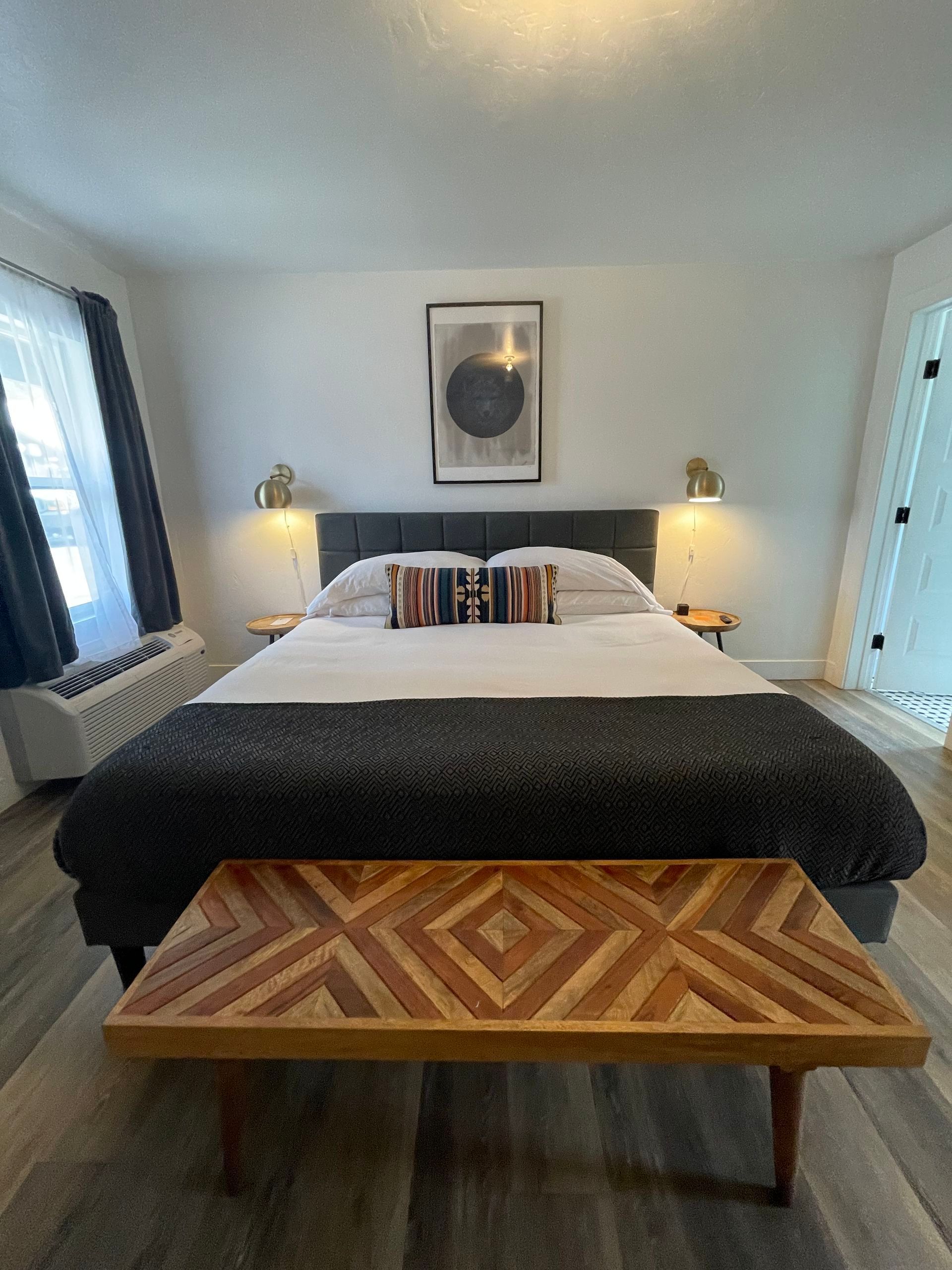 Bedroom with bed, patterned bench, artwork, and lamps.