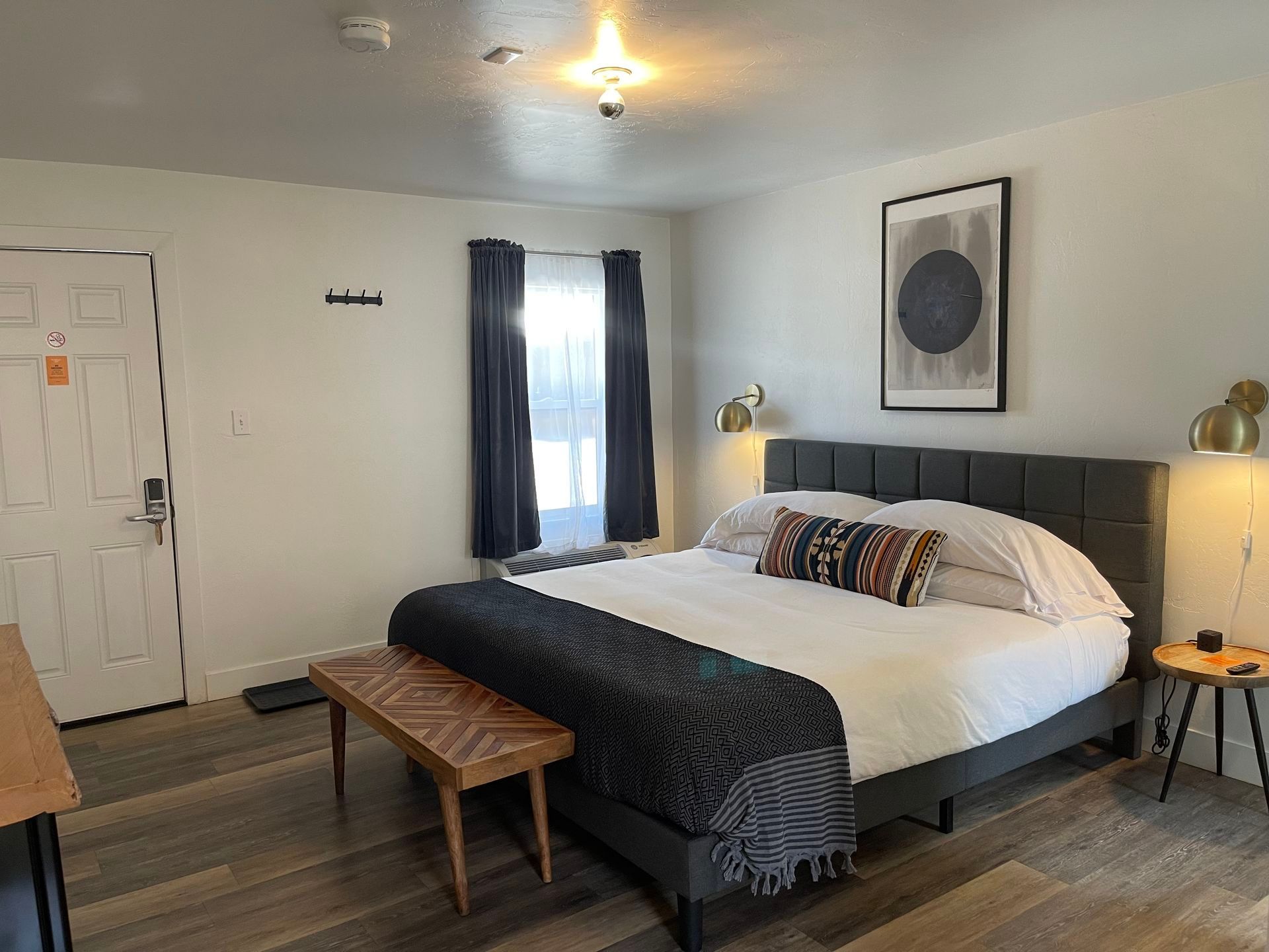 Bedroom with gray bed, wooden bench, artwork, and side table with a lamp.