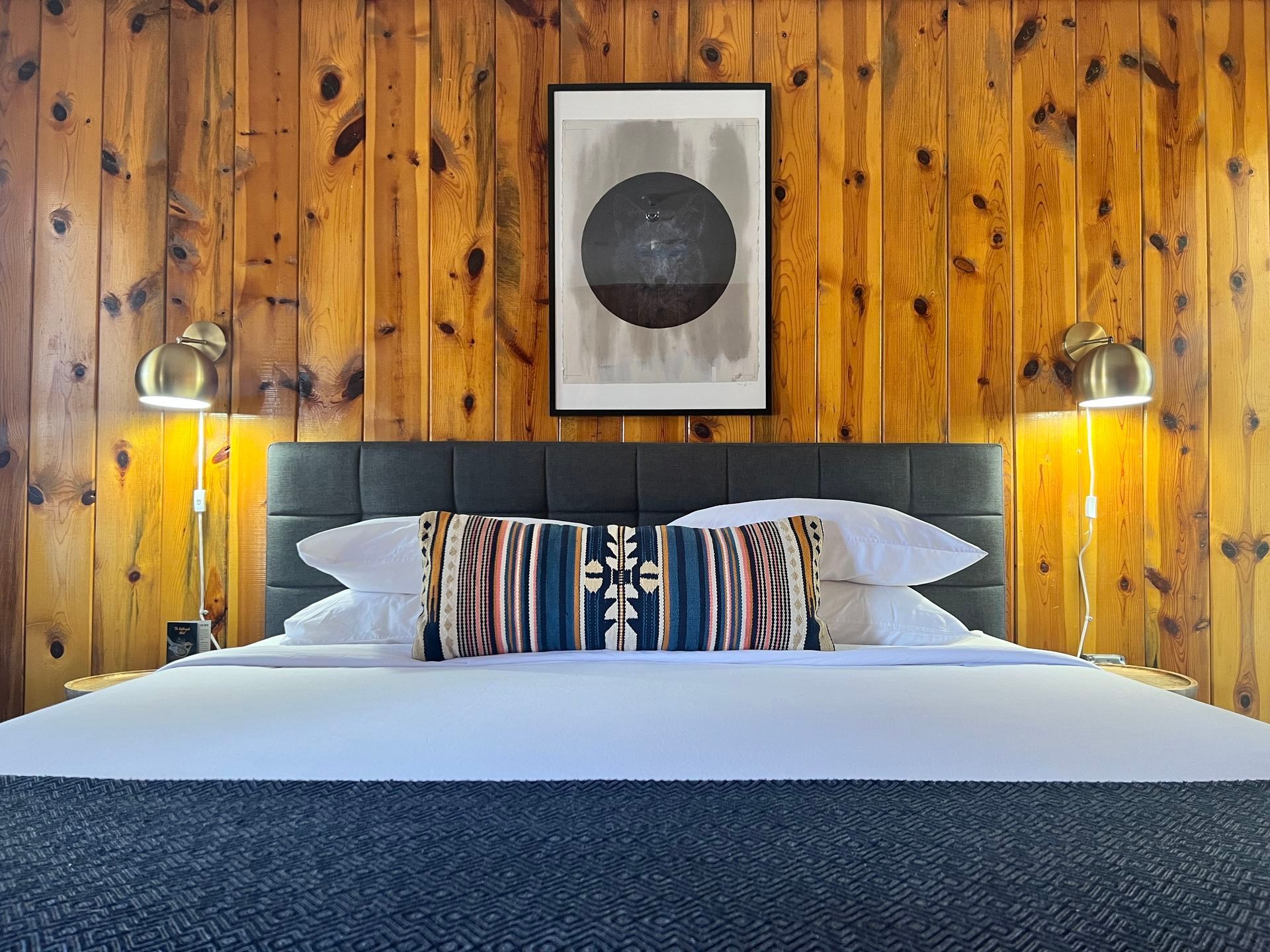 A bed in a room with a wood-paneled wall, pillows, and art. Two bedside lamps flank the headboard.