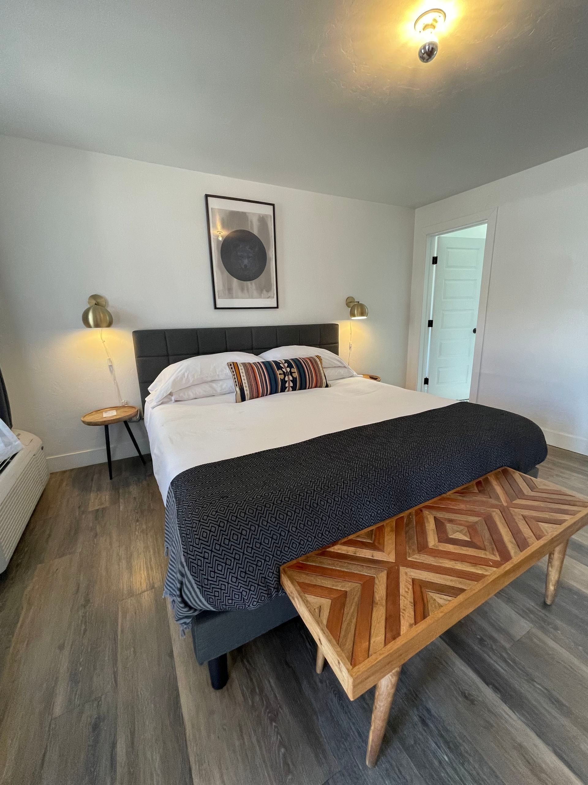 Bedroom with gray bed, patterned throw, wooden bench, and wall art.