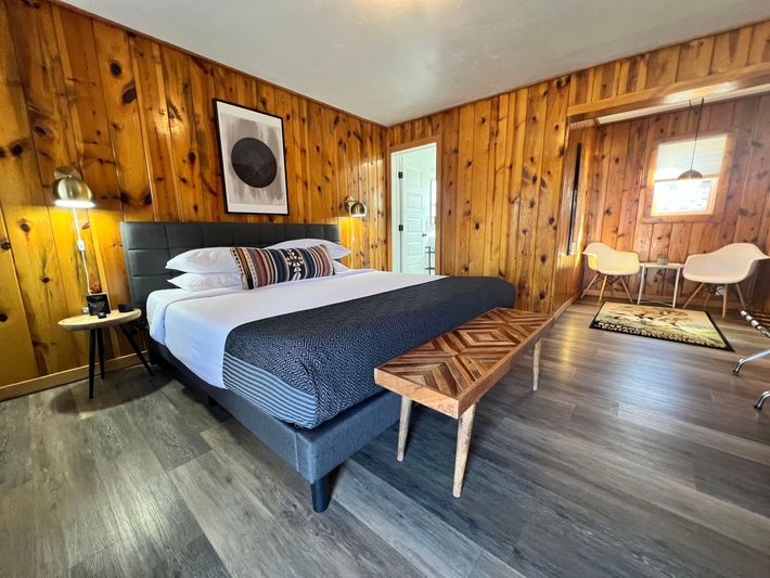 Bedroom with wood panel walls, a gray bed, and a wooden bench at the foot of the bed.