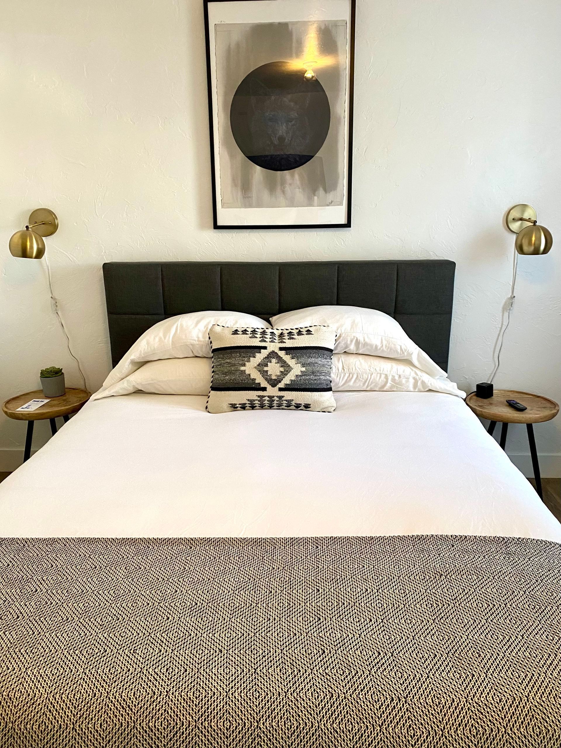 Bedroom with a bed, artwork, and bedside tables. The bed has a decorative throw and pillows.