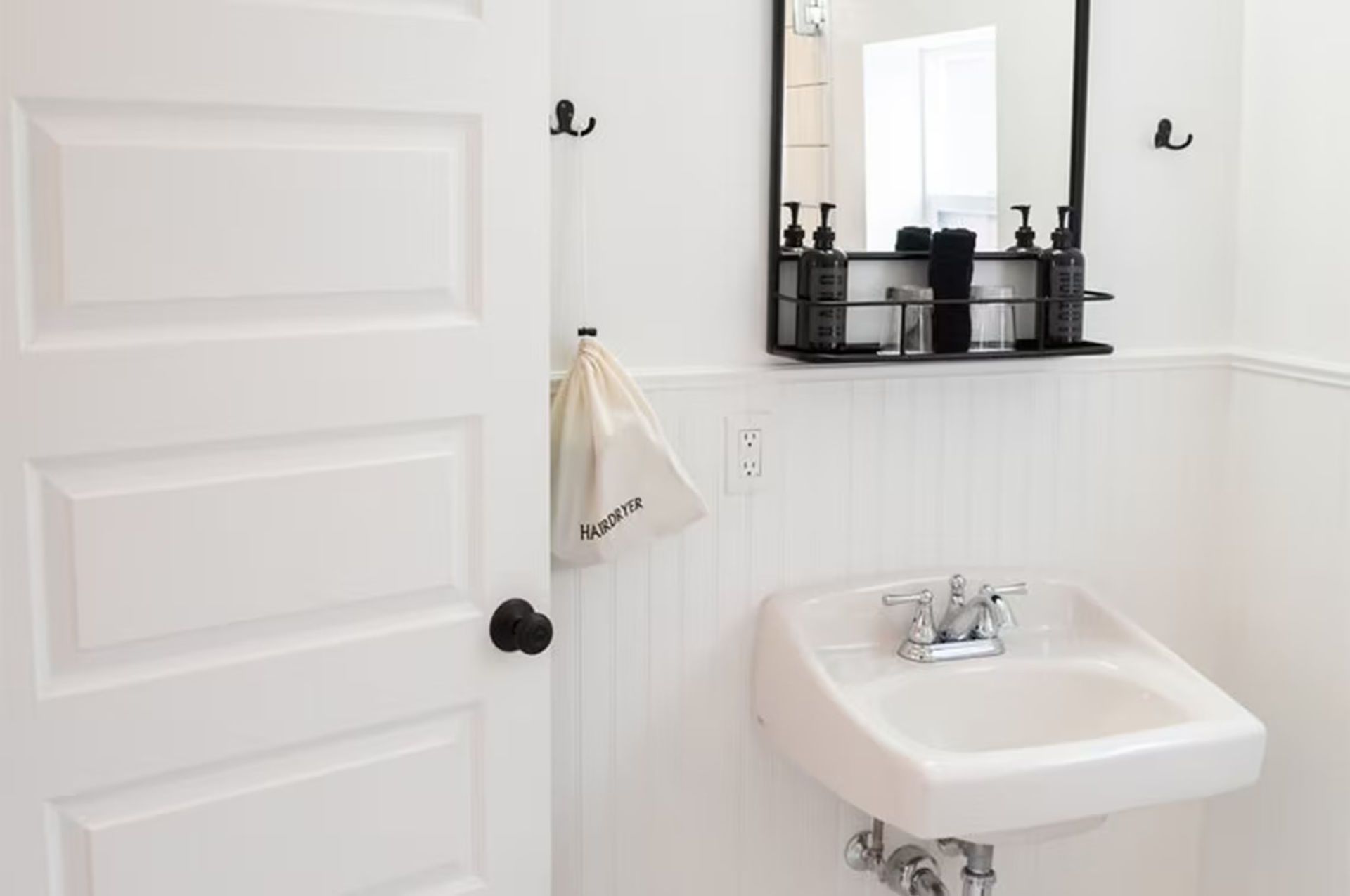 White bathroom with a sink, mirror, and a partially visible door.