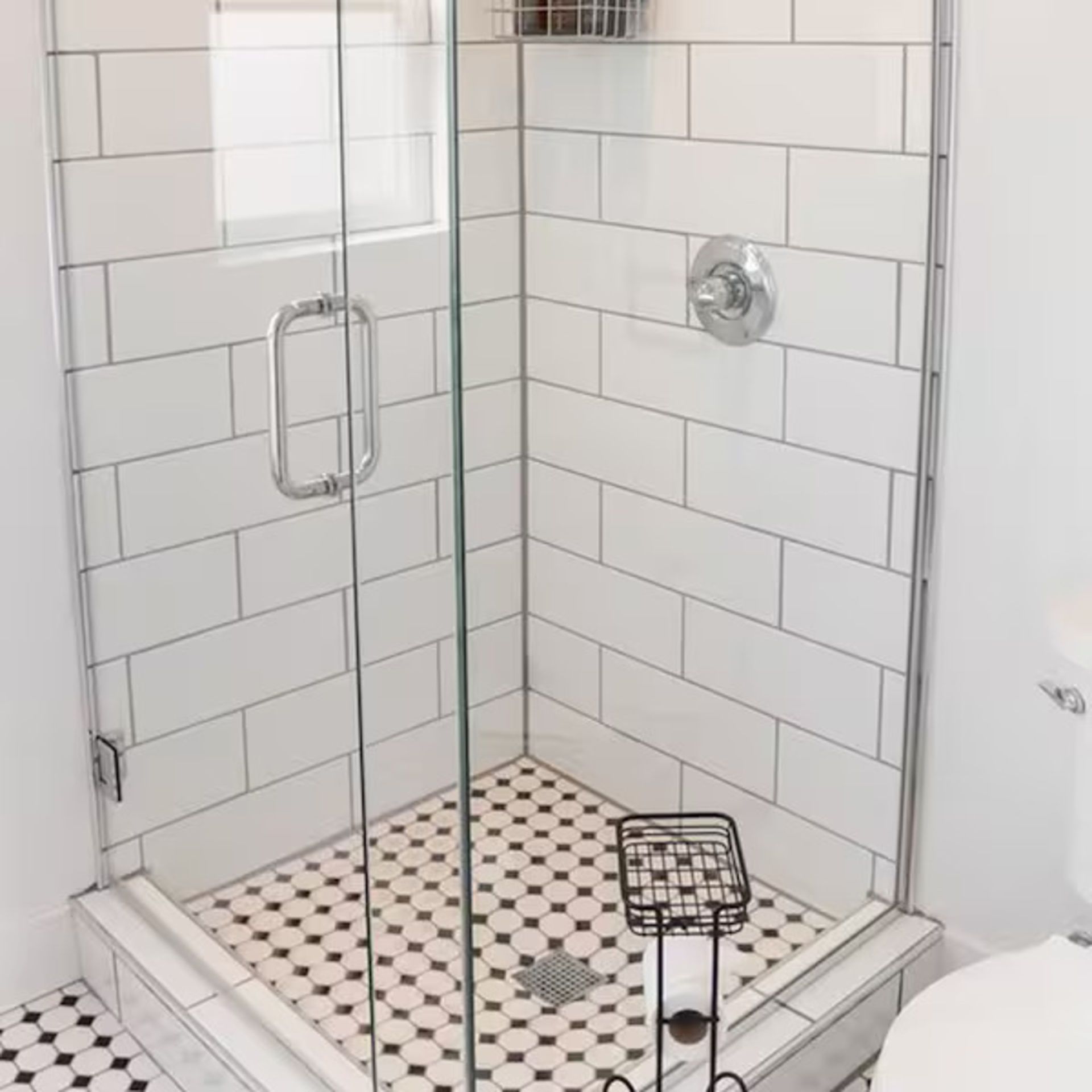 Tiled shower with glass door, black and white patterned floor. Chrome fixtures, white subway tile walls.